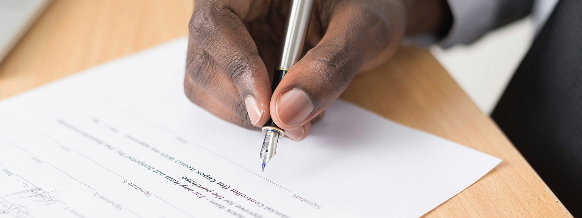 Close up photo of a persons hands holding a fountain pen as they sign a legal document.