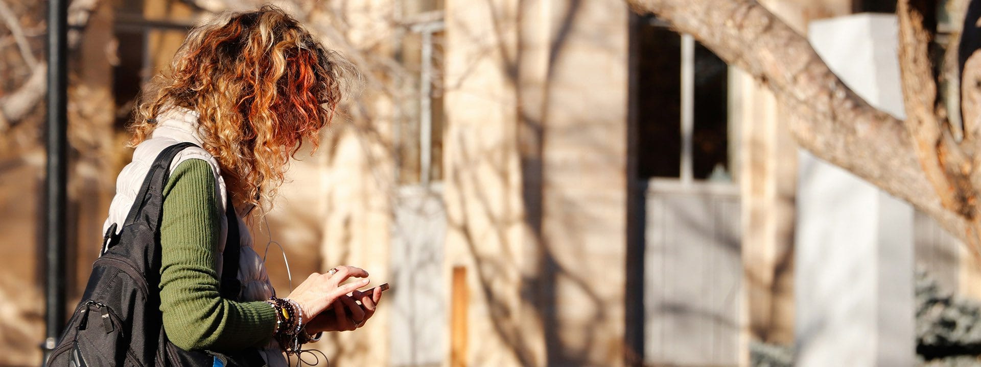 A person looks down at their phone while standing outside